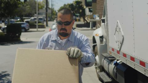 man with glasses next to truck pushing a dolly with a box on it