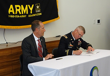 two men at a table, one is signing a document 