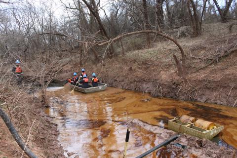 Emergency response oil cleanup. Crew in a boat and gear going down a brown river